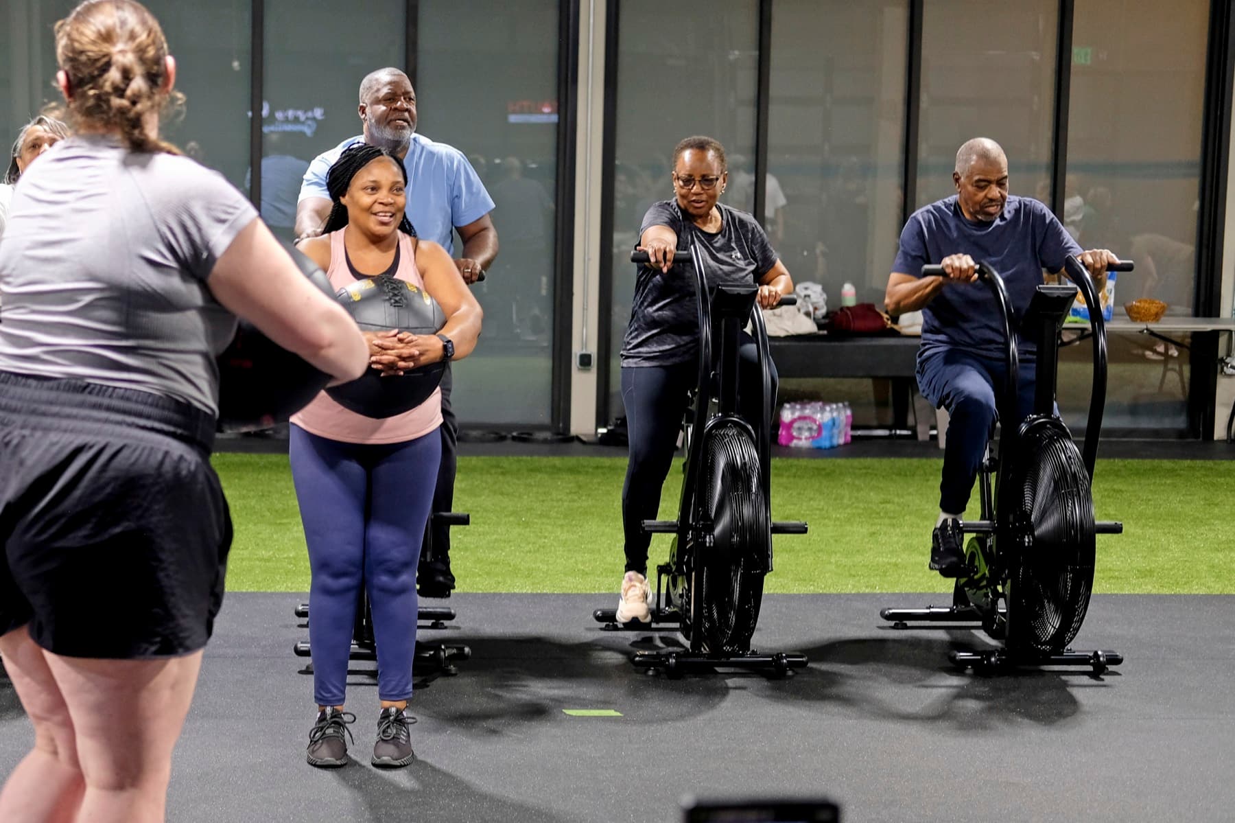 A mixed group of Fitness 300 members training together on the turf and air bikes