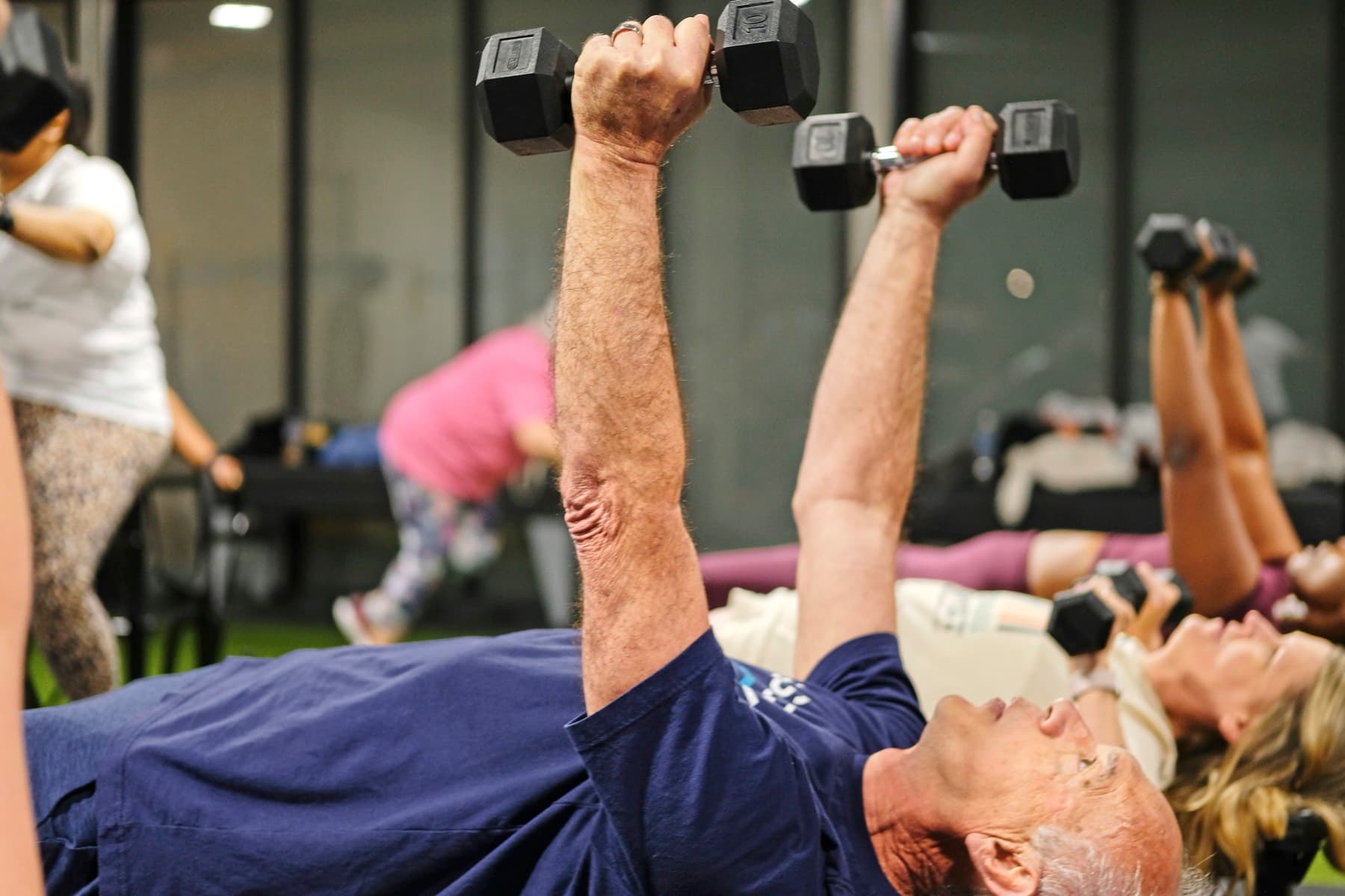 Two older members pressing dumbbells on benches during a Fitness 300 class